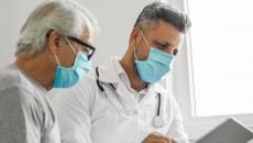 A medical professional and a patient talking to another provider using a tablet. 