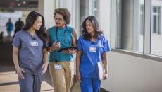 Three healthcare providers walking through a hall while looking at a tablet