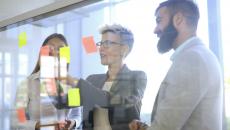 Three people standing in front of a board looking at post-its on a wall