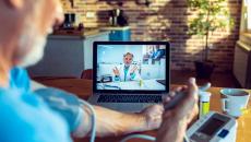 An older man talking to a provider via telehealth while checking his blood pressure